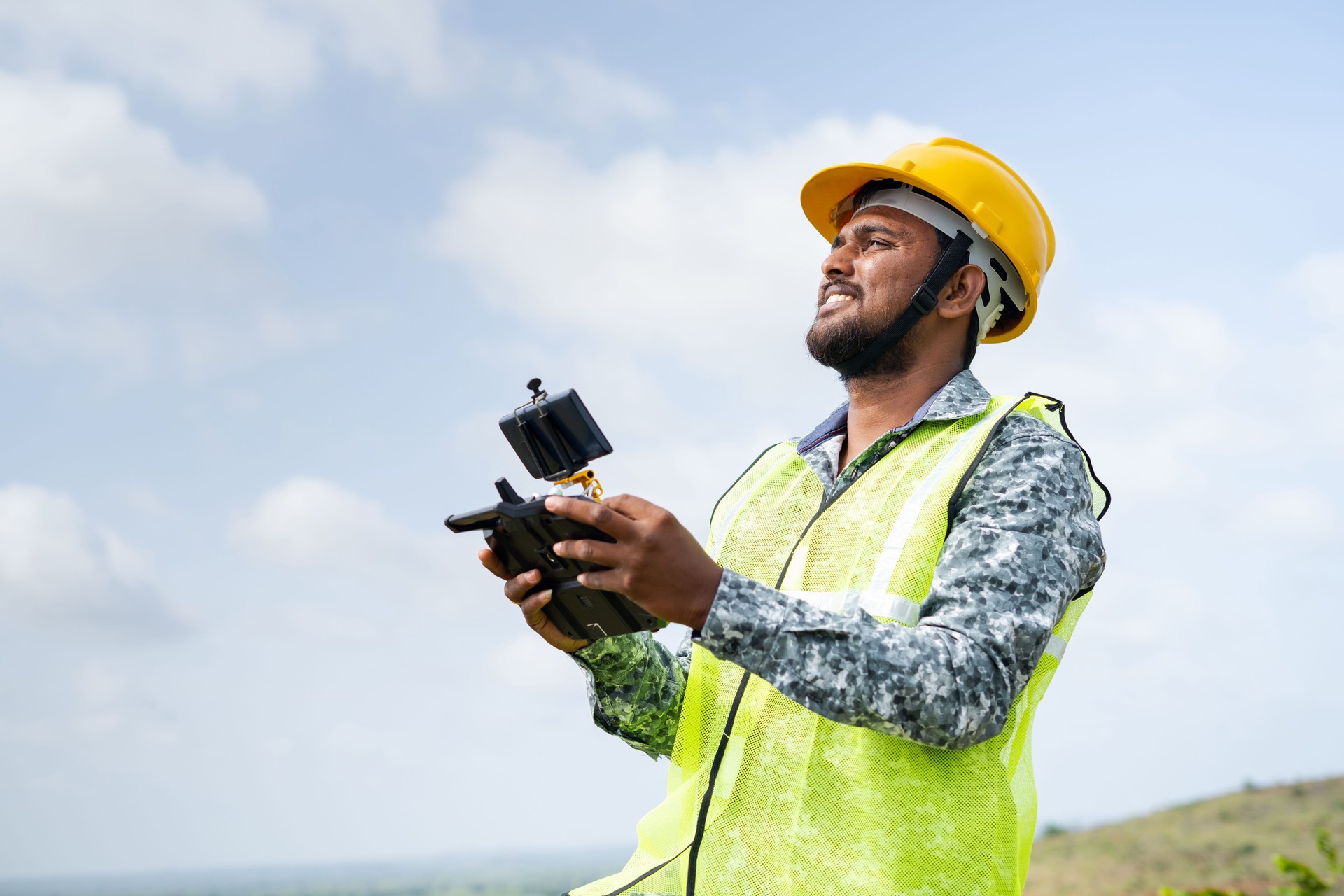 Drone pilot with safety helmet operating drone using remote controller - concept of engineer using drone technology to survey land.